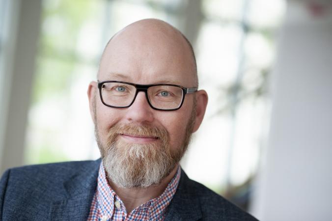 Jonas är snaggad och har skägg. Han bär glasögon med mörk båge.