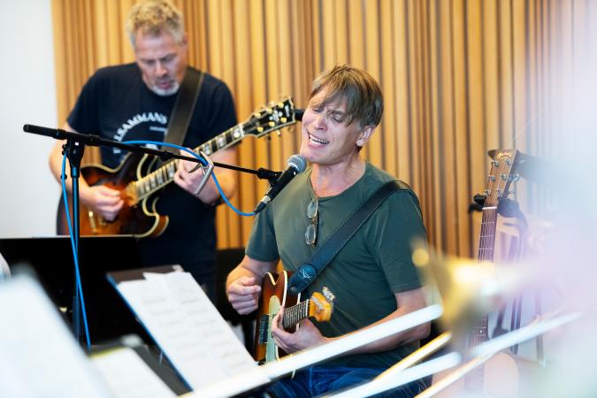 Magnus och Norrbotten Big Band repeterar inför turné. Magnus spelar gitarr sjunger och bakom honom står gitarristen.