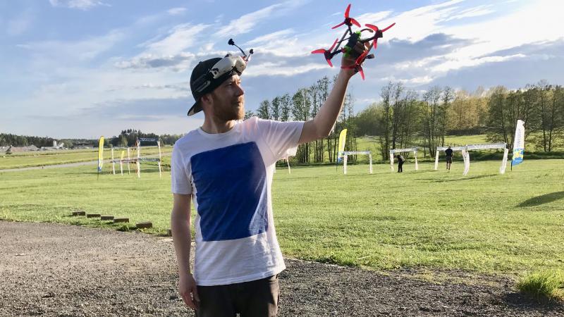 En kille i vit t-shirt håller en drönare i handen. Den ser ut som en stor spindel, eller ett rymdskepp med smala ben.