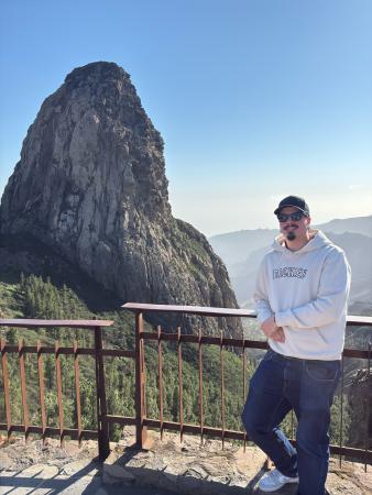 En ung  man i vit tröja, svarta byxor och keps framför en bergsformation på Teneriffa. Han bär ett par svarta Ray Ban smartglasögon med kamera, högtalare och mikrofon i skalmen. Genom röstkommandon kan omgivningarna syntolkas, fotograferas eller filmas.