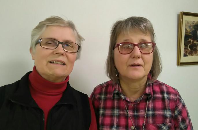 En bröstbild på Margareta Pettersson och Hjördis Lindström. Margareta har kort hår, glasögon och en röd polotröja under en mörk väst. Hjördis har halvlångt hår i page, glasögon och en röd- och gråsvartrutig skjorta