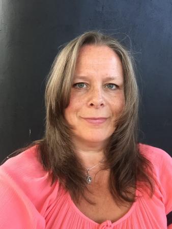 Eva Marie klädd i aprikosfärgad topp har långt mörkt, uppklippt hår. Hon ser glad ut.
