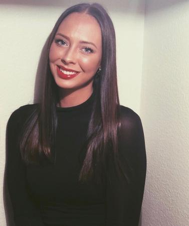 Rebecca har långt mörkt hår och bär en svart tröja. Hon ser glad ut på bilden.
