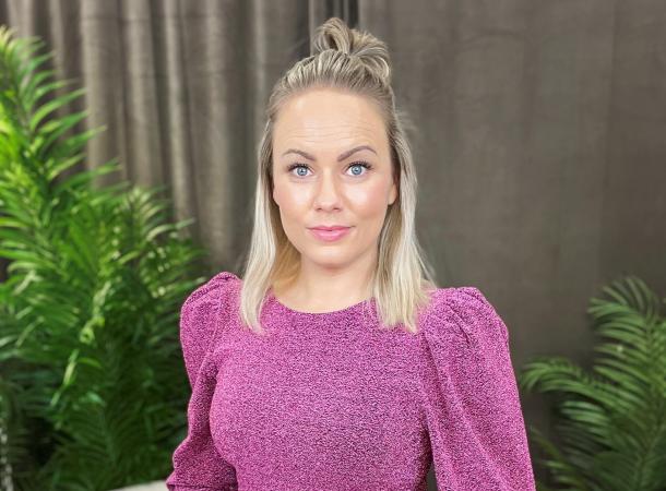 Elisabeth är blond med långt hår och luggen uppsatt. Hon bär en tröja med puffärmar i en rosa nyans