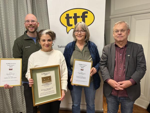 Aziza har lockigt mörkt hår med en grå slinga längst fram. Bakom hennes står de två hederspristagarna Åsa Kjellman Irici och Henrik Jansson samt prisutdelaren Bert Sundström