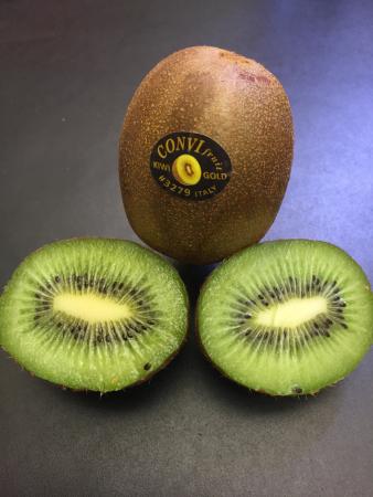 Kiwi, en brun, hårig äggformad frukt står upp bakom den genomskurna frukten; grön/vit med svarta små frön.