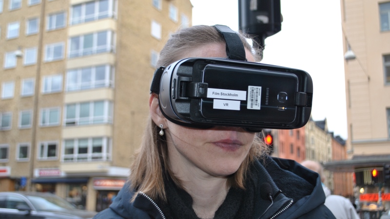 Annika har en svart VR-kamera fastspänd på huvudet och står uthomhus i stadsmiljö. Hon ser bestämd ut.
