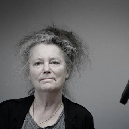 Kerstin har grått hår uppsatt på huvudet. Hon har en svart kavaj över en grå tröja. Hon ser stolt ut.