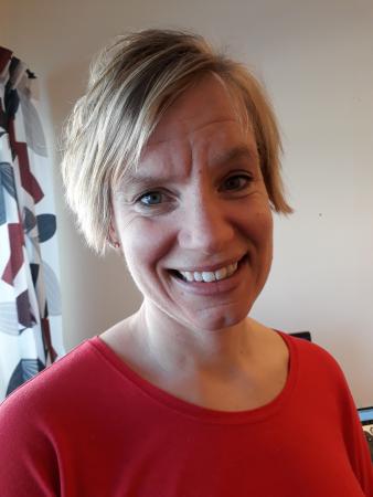 Karolina har ljust hår klippt i page och bär en röd tröja. Hon ser glad ut på bilden