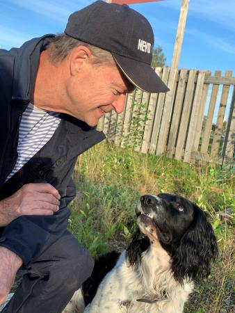 Den svartvita springerspanieln tittar kärleksfullt på sin husse Mikael som har grå kepa och grå jacka. Håret är kortsnaggat. Han ser glad ut.