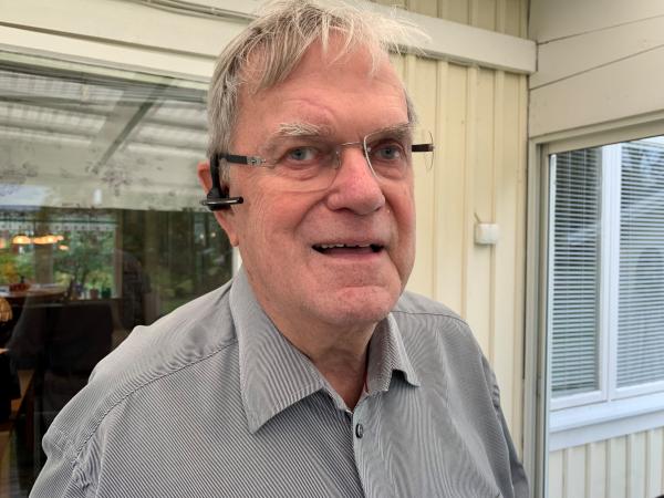 PO har grått kort hår, glasögon och ett svart headset. Han ser glad ut.