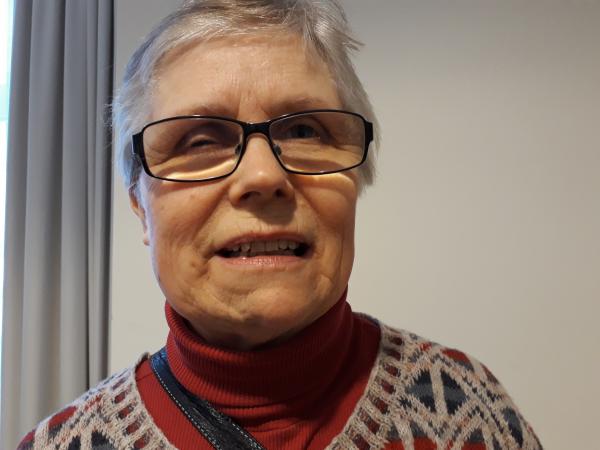 Margareta Pettersson har kortklippt grått hår och rektangulära glasögon med tunna svarta bågar. Hon har en rödorange polotröja och en grå, mönstrad kofta.
