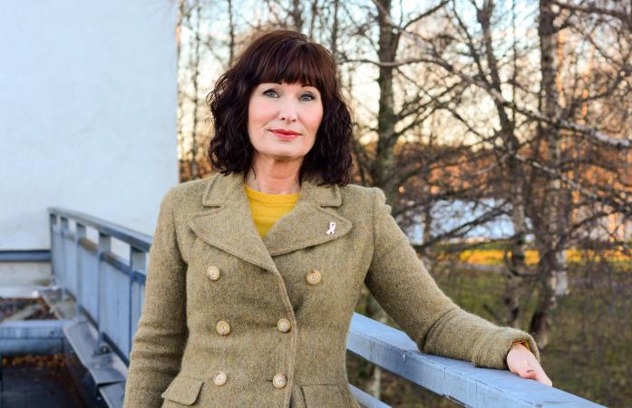 Therese har rött axellångt hår. Hon har en beigegrön jacka och står ute en höstdag