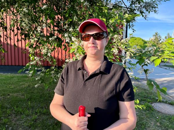 Evelina har en kepa och bär solglasögon. Hon står framför en blommande hägg.