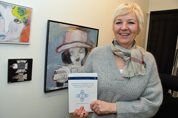Sarianne har kort, ljust hår och ser jätteglad ut. På bilden håller hon i sin doktorsavhandling.