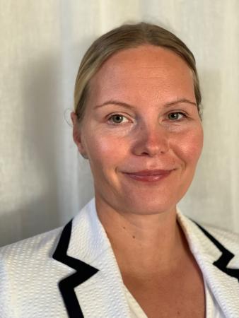 Marianne har mellanbrunt uppsatt hår och bär vit kavaj med svarta rand runt kragen