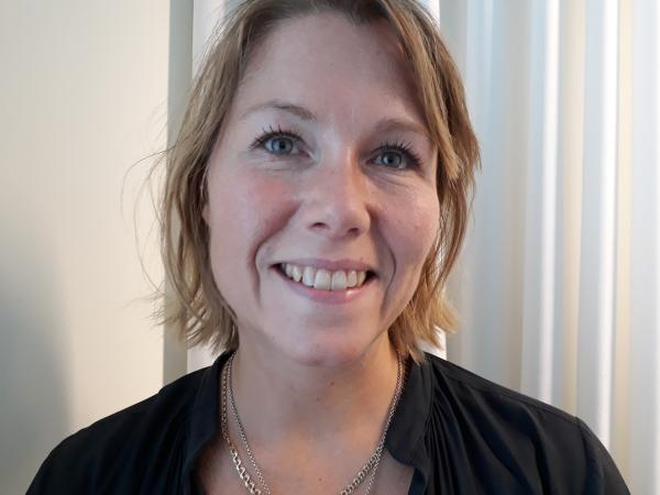Linda Nygren har halvlångt, rödblondt hår. Hon har en mörk blus och två smala halsband.