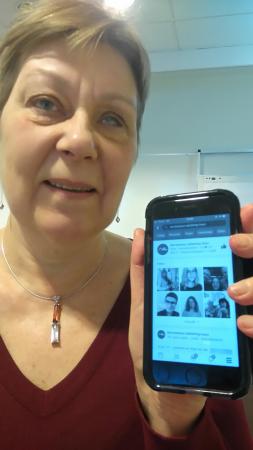 Karin har kort, mellanblont hår och håller upp en mobil.