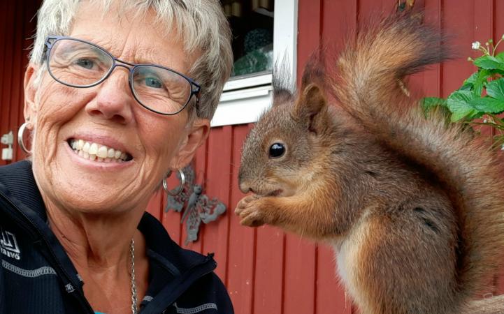Karin syns leende bredvid an ekorre som sitter bredvid henne och äter ett solrosfrö.