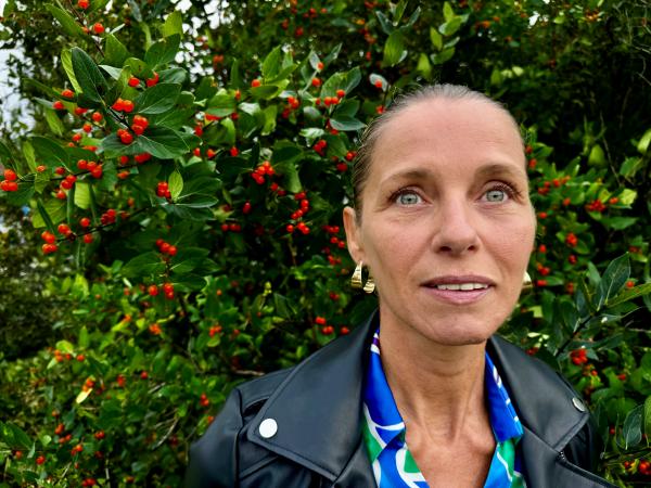 Andrea har håret uppsatt och bär guldfärgade örhängen. Hon står framför en buske med röda bär och har en blå-grönmönstrad blus och en svart skinnjacka. Hon ser glad och lite eftertänksam ut när hon fäster den gröna blicken i fjärran.