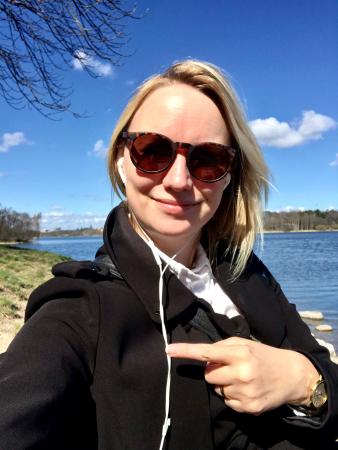 Linda syns framför vatten på prommenad med musik i hörlurarna. Hon har ljus hår ner till axlarna och bär solglasögon. Hon ser nöjd ut och pekar åt sidan.