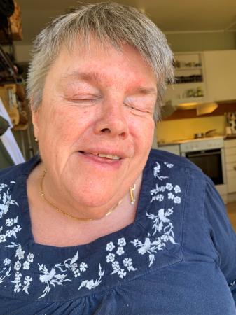 Anita har grått kort hår och har en blå tröja. Hon ser glad ut på bilden.