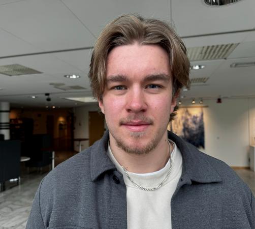 Hugo har en vit tröja och grå skjorta. Han har lite åt hockeyfrilla och getskägg. Han har blå ögon. Hugo Rova