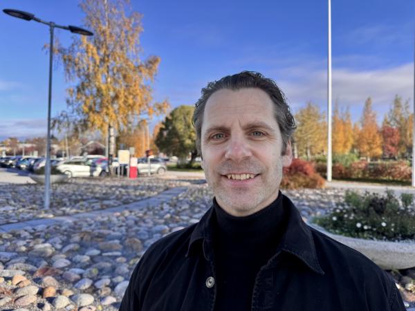 Olof har mörkt bakåtkammat hår och bär en svart jacka. Han ser glad ut. Olof Westring